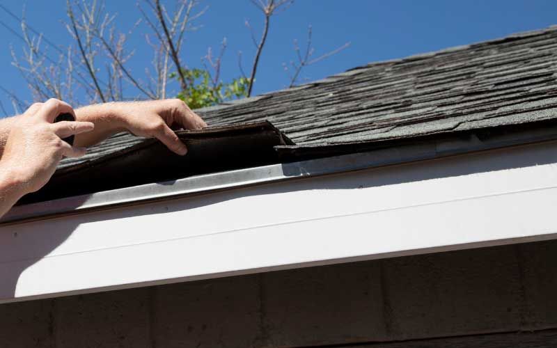Person inspecting roof shingles.